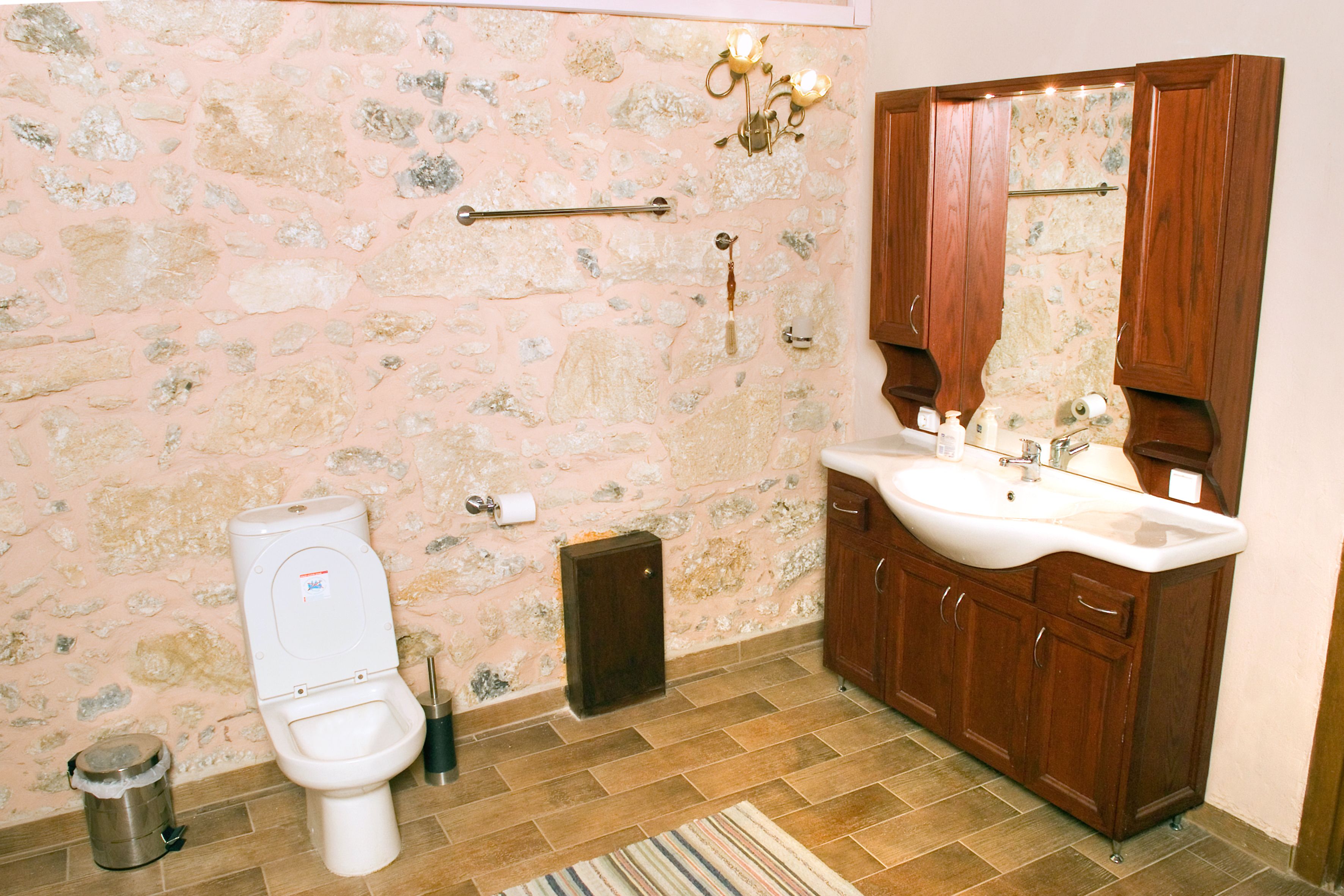 Un baño con pared de piedra, inodoro, lavamanos y armarios de madera.