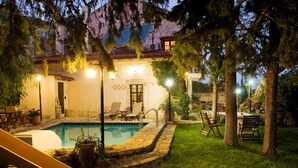Un área de piscina con tobogán, sillones de descanso y una piscina de piedra rodeada de césped y árboles.