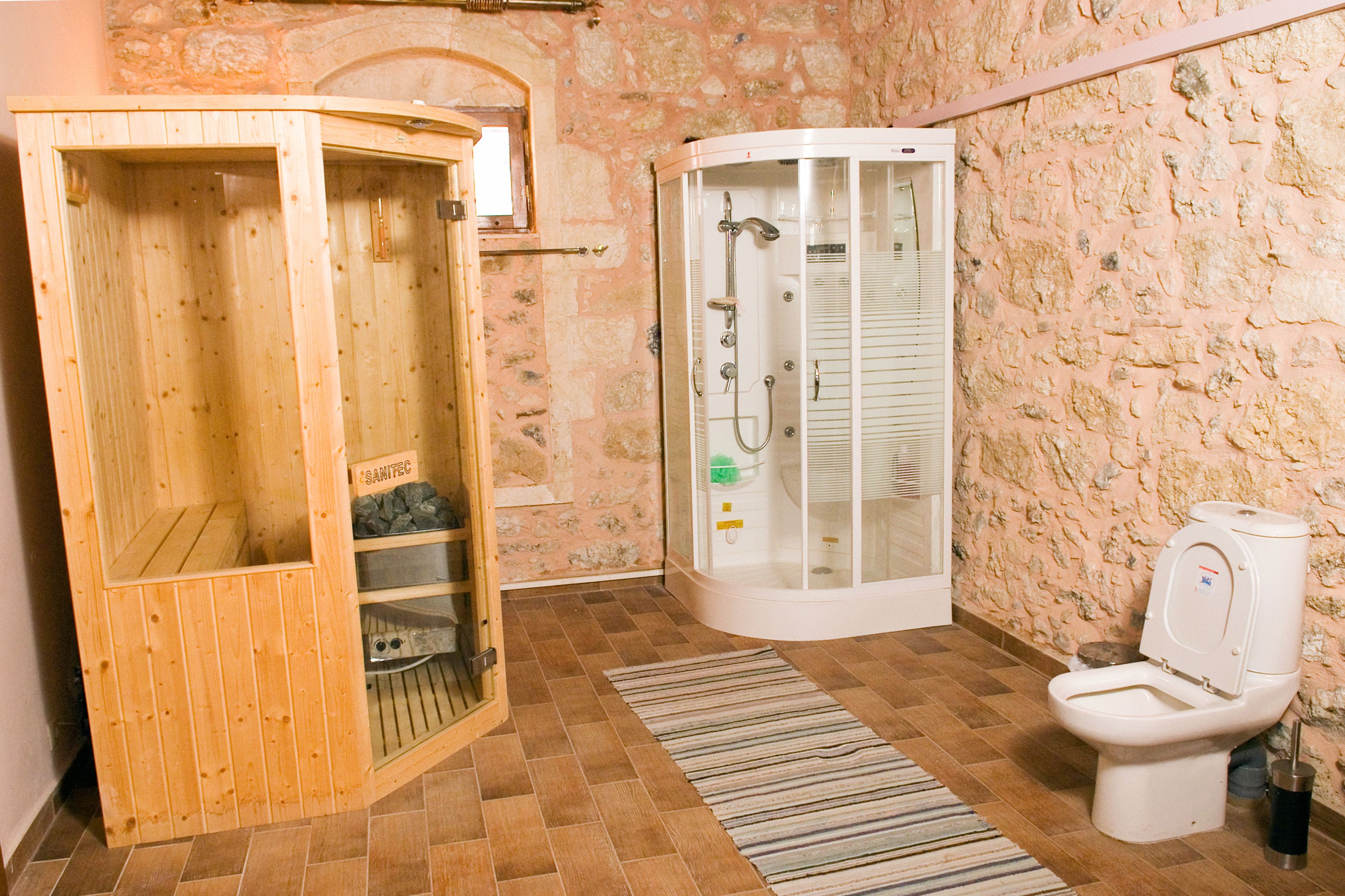 A wooden sauna and a glass-enclosed shower in a room with stone walls and a tiled floor.
