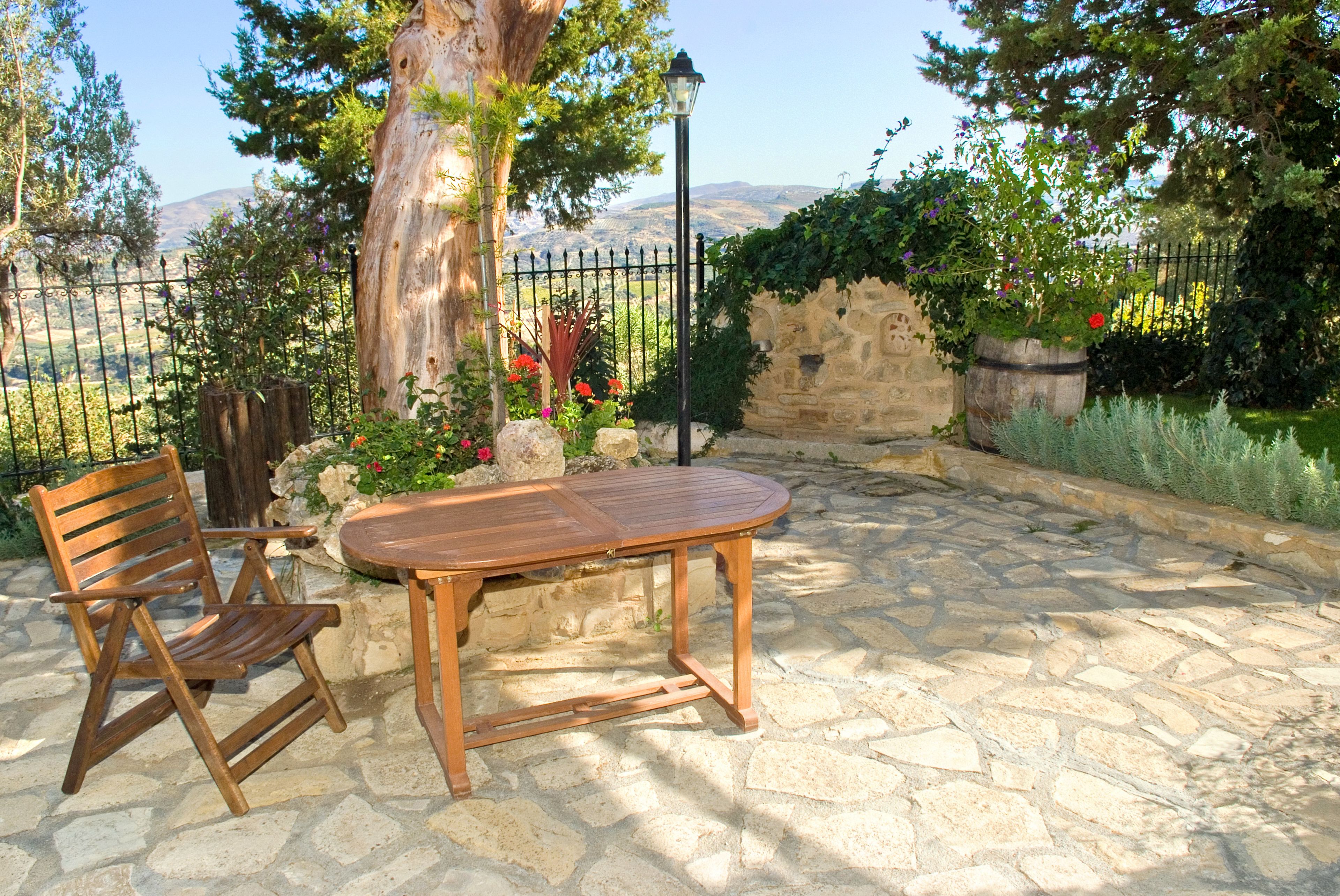 A stone patio with a wooden table and chairs, surrounded by a stone wall and a metal fence.