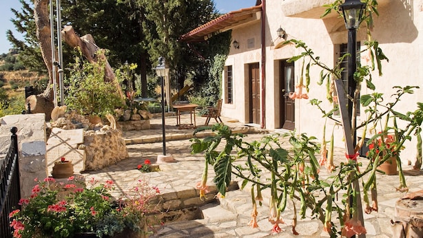 Un patio de piedra con una fuente rústica, plantas en macetas y una mesa de madera.