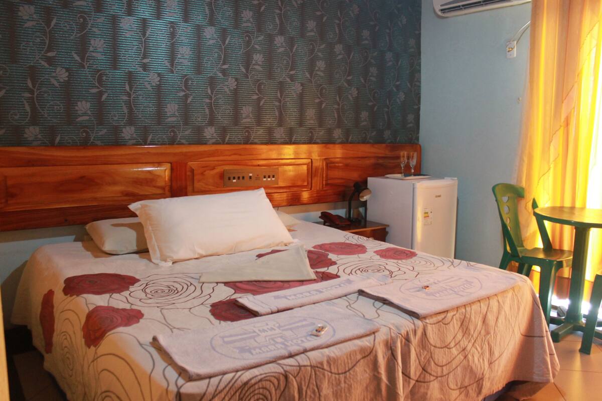 A hotel room with a wooden headboard, a bed with floral bedding, a small table, and a chair.
