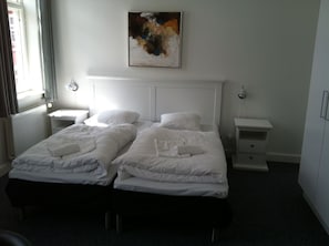 A hotel room with two beds, a painting on the wall, a window with curtains, and a radiator. - Hotel Posthuzed (Ronne)
