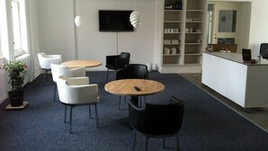 Um espaço de escritório moderno com mesas redondas, cadeiras pretas e brancas, uma televisão de tela plana e uma estante com diversos objetos.
