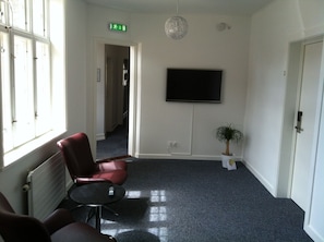A room with a red chair, a small table, a potted plant, a flat-screen TV mounted on the wall, and a radiator. - Hotel Posthuzed (Ronne)