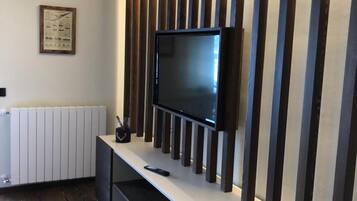Una sala moderna con un televisor de pantalla plana montado en una pared con listones de madera verticales, un radiador blanco y un cuadro enmarcado.