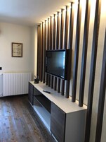 Una sala moderna con un televisor de pantalla plana montado en una pared con listones de madera verticales, un radiador blanco y un cuadro enmarcado.
