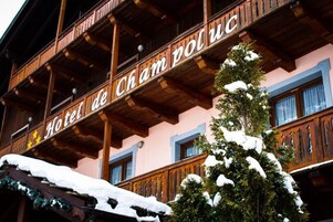 Hotel con fachada de madera y balcones, nieve en el tejado y árboles, y un letrero que dice 'Hotel de Cham de Ross'.