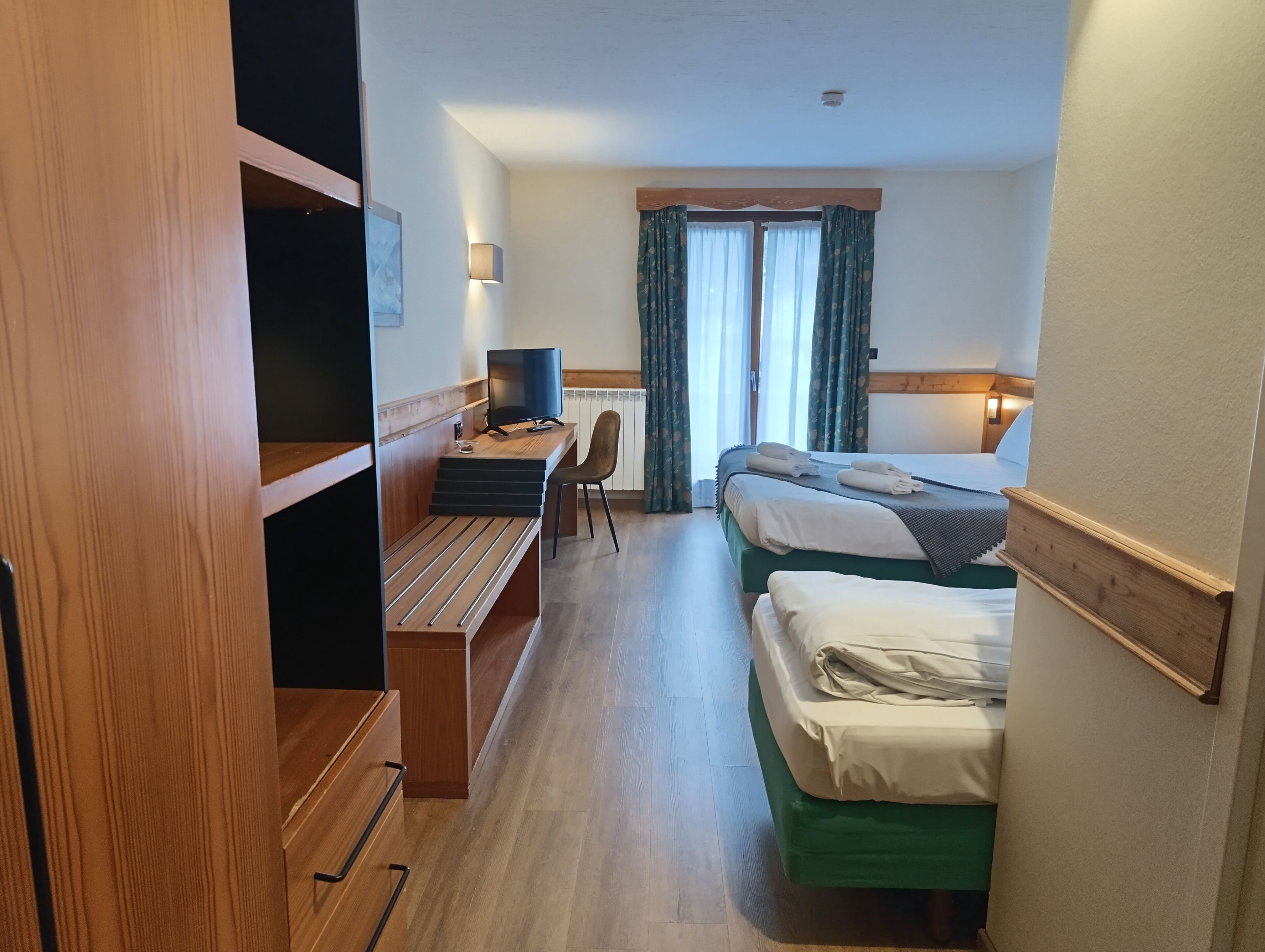 Habitació d'hotel amb escriptori, televisió, dos llits i finestra amb cortines.