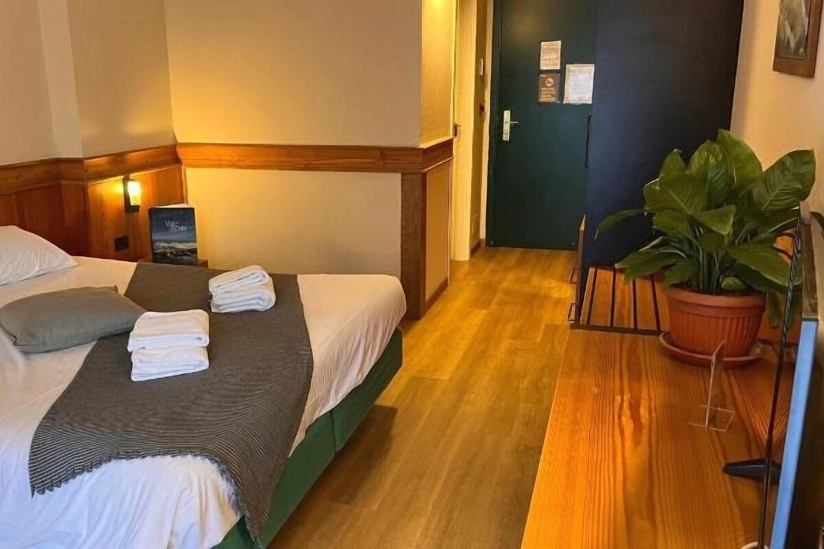 A hotel room with two beds, a wooden floor, a potted plant, and a door in the background.