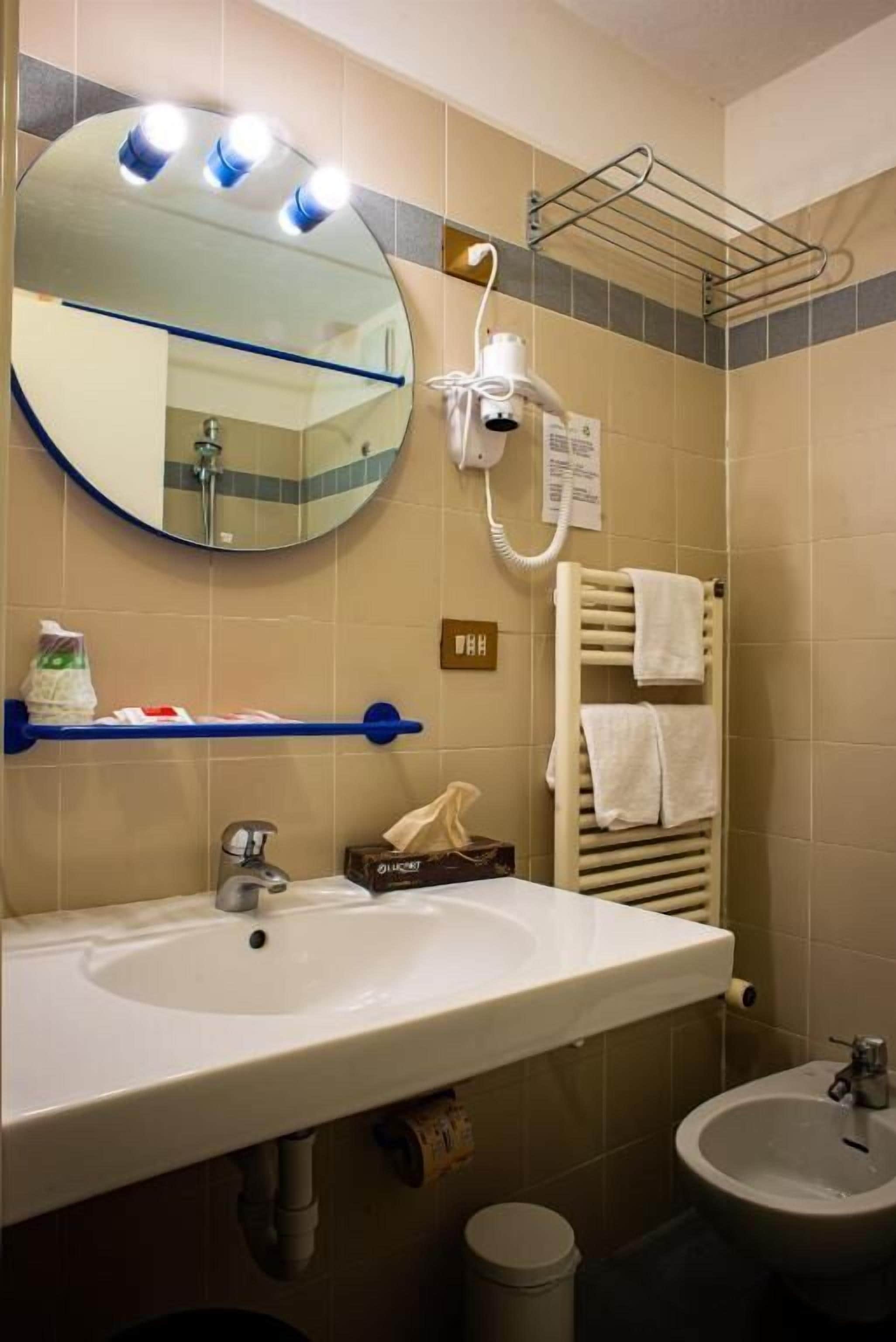 A bathroom with a round mirror, a sink, a bidet, and a towel rack.