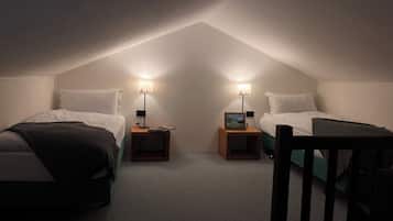 Um pequeno quarto de sótão com pouca luz, com duas camas, cada uma com mesa de cabeceira e luminária.