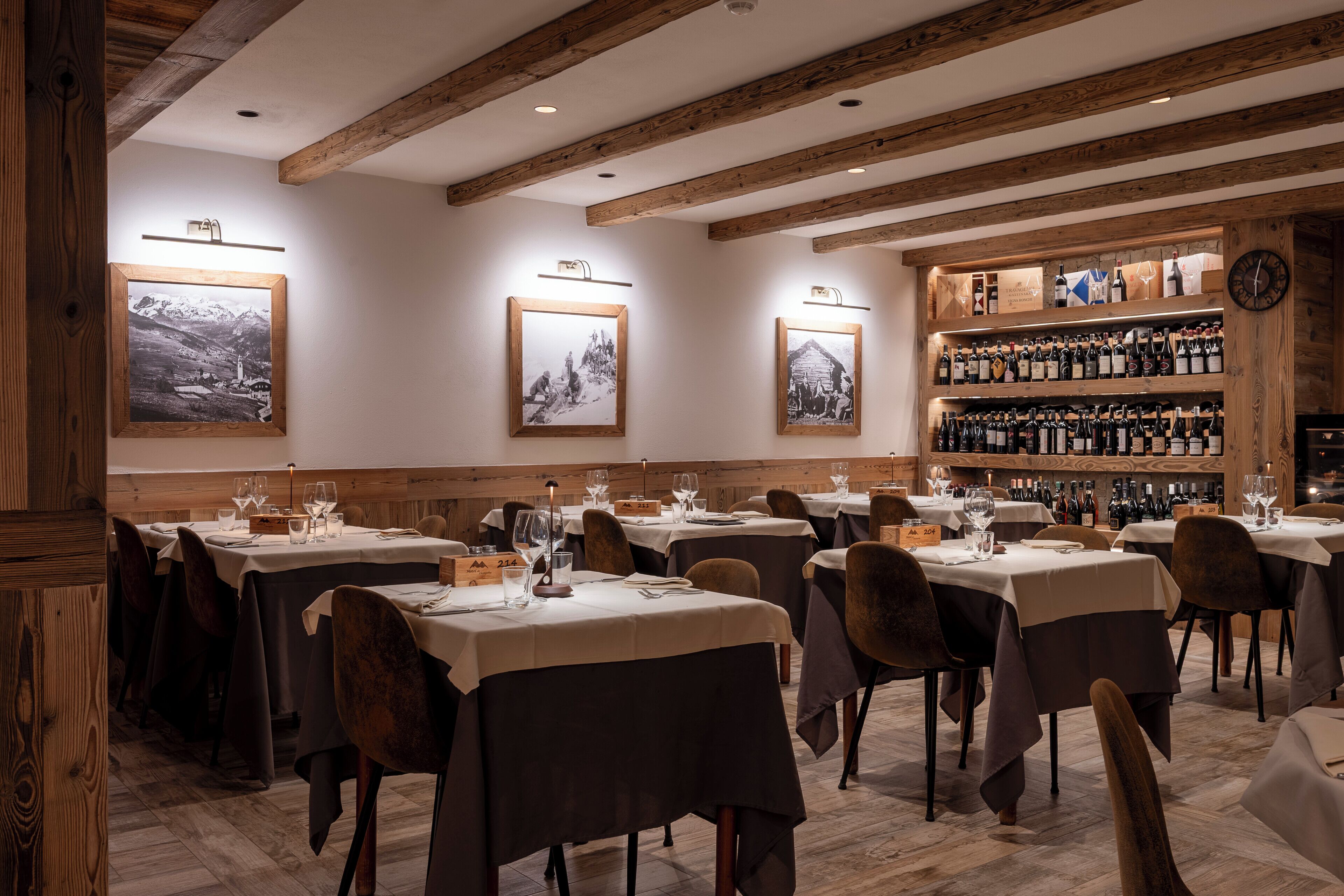 Interior de restaurante con vigas de madera, mesas con manteles blancos y botellas de vino en estanterías.