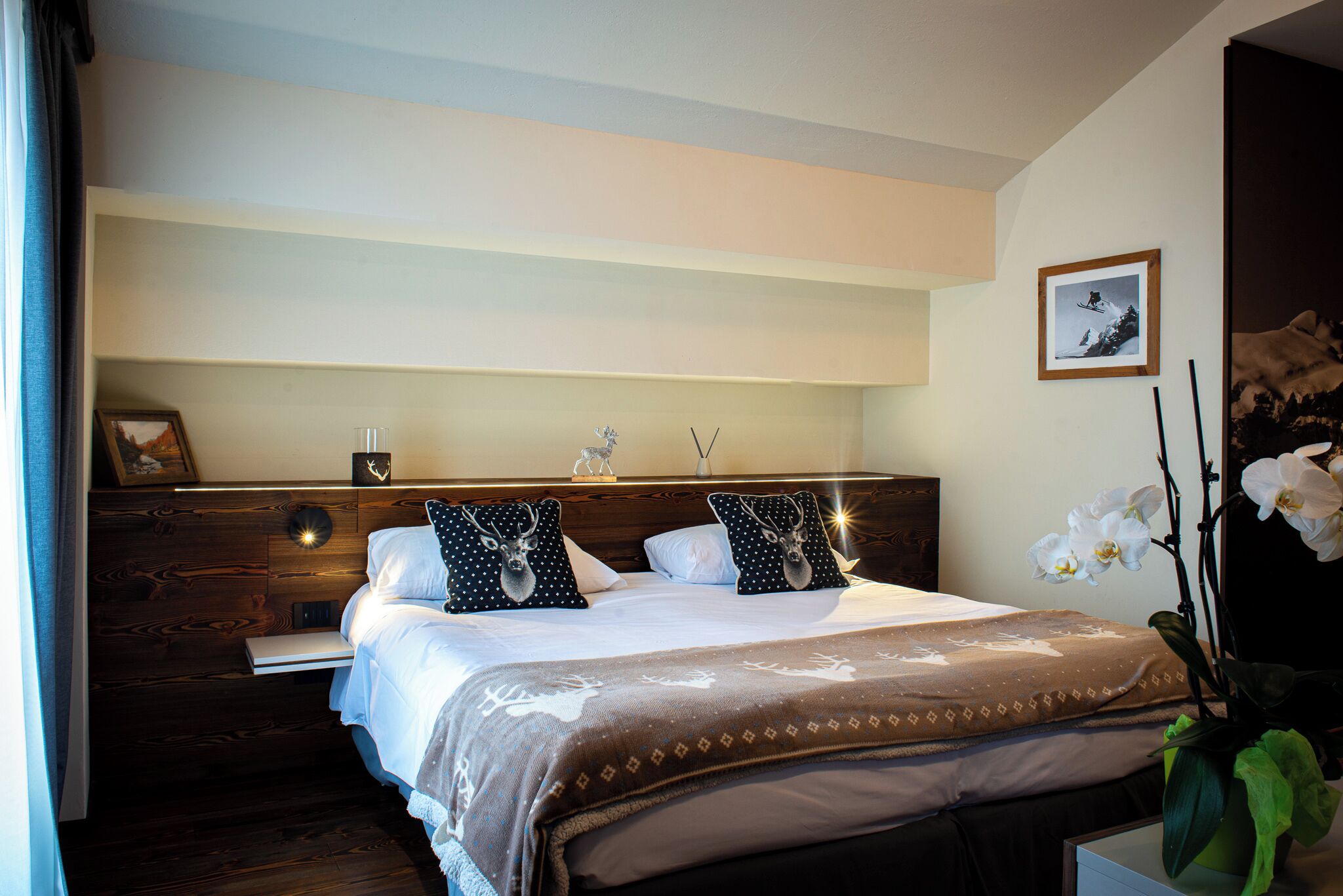 A hotel room with a large bed, wooden headboard, bedside tables, a framed picture on the wall, and a vase with flowers.