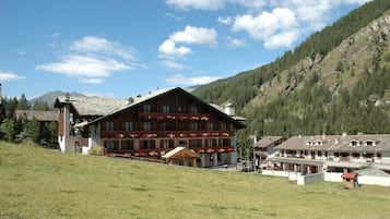 Ein großes Gebäude mit mehreren Balkonen, umgeben von einer grünen Fläche und Bergen im Hintergrund.