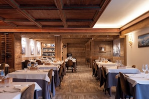 Un restaurante con interiores de madera, varias mesas preparadas para comer y una estantería con vino de fondo.