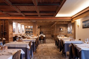 Un restaurante con interiores de madera, varias mesas preparadas para comer y una estantería con vino de fondo.