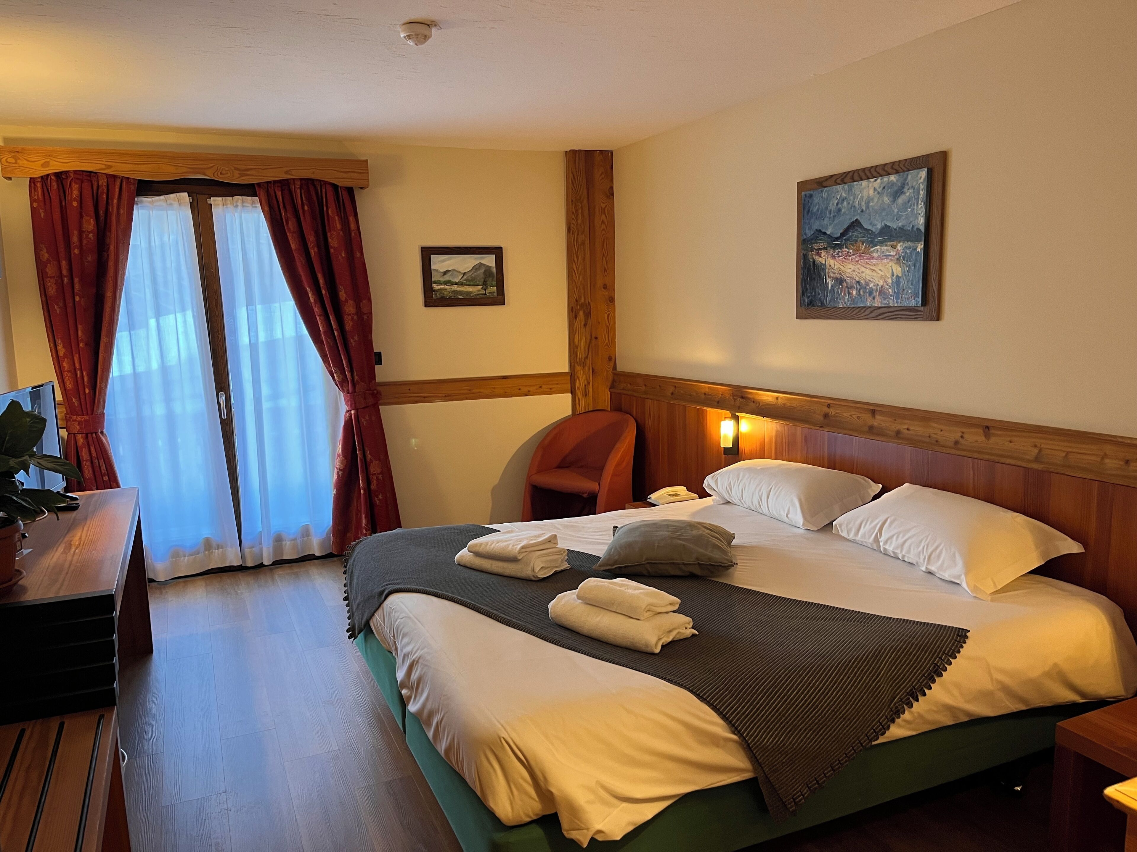 A hotel room with a bed, a desk, a chair, and a painting on the wall.