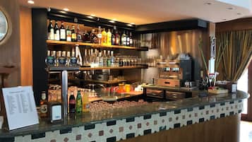 Un espace bar avec des étagères remplies de bouteilles d’alcool, de verres et une machine à café.