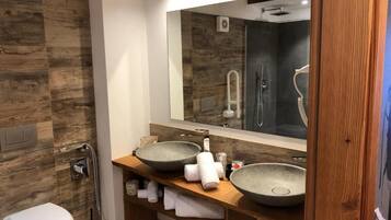 A modern bathroom with a wooden wall, a large mirror, two vessel sinks, a toilet, and a shower area.