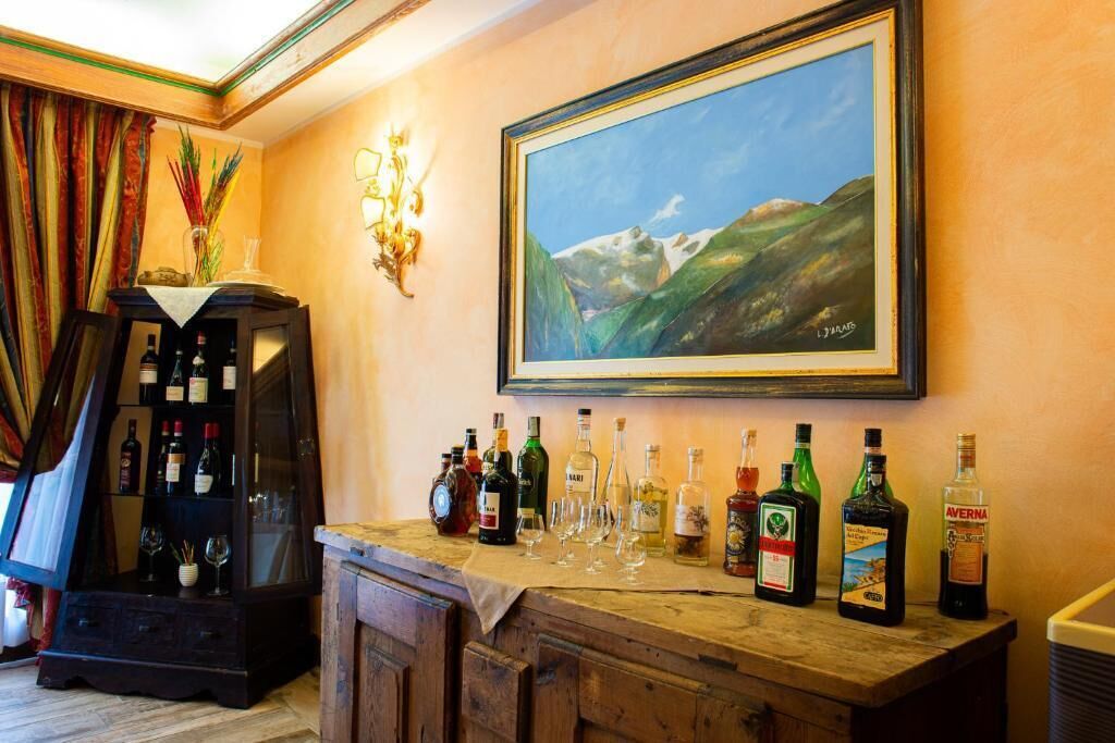 Zona de bar con mostrador de madera, botellas de licores y copas de vino. Un cuadro enmarco con un paisaje de montaña cuelga sobre el mostrador.