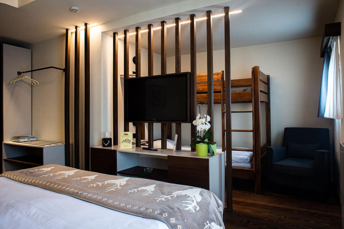 A hotel room with a bed, a desk with a TV, a bunk bed, a chair, and a wardrobe.
