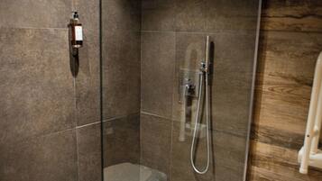 A modern bathroom with a glass-enclosed shower, a toilet, and a towel on the floor.