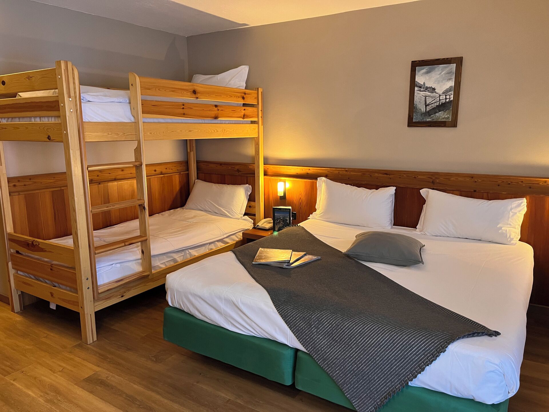Habitación de hotel con literas, una cama individual y una mesita de noche con lámpara.