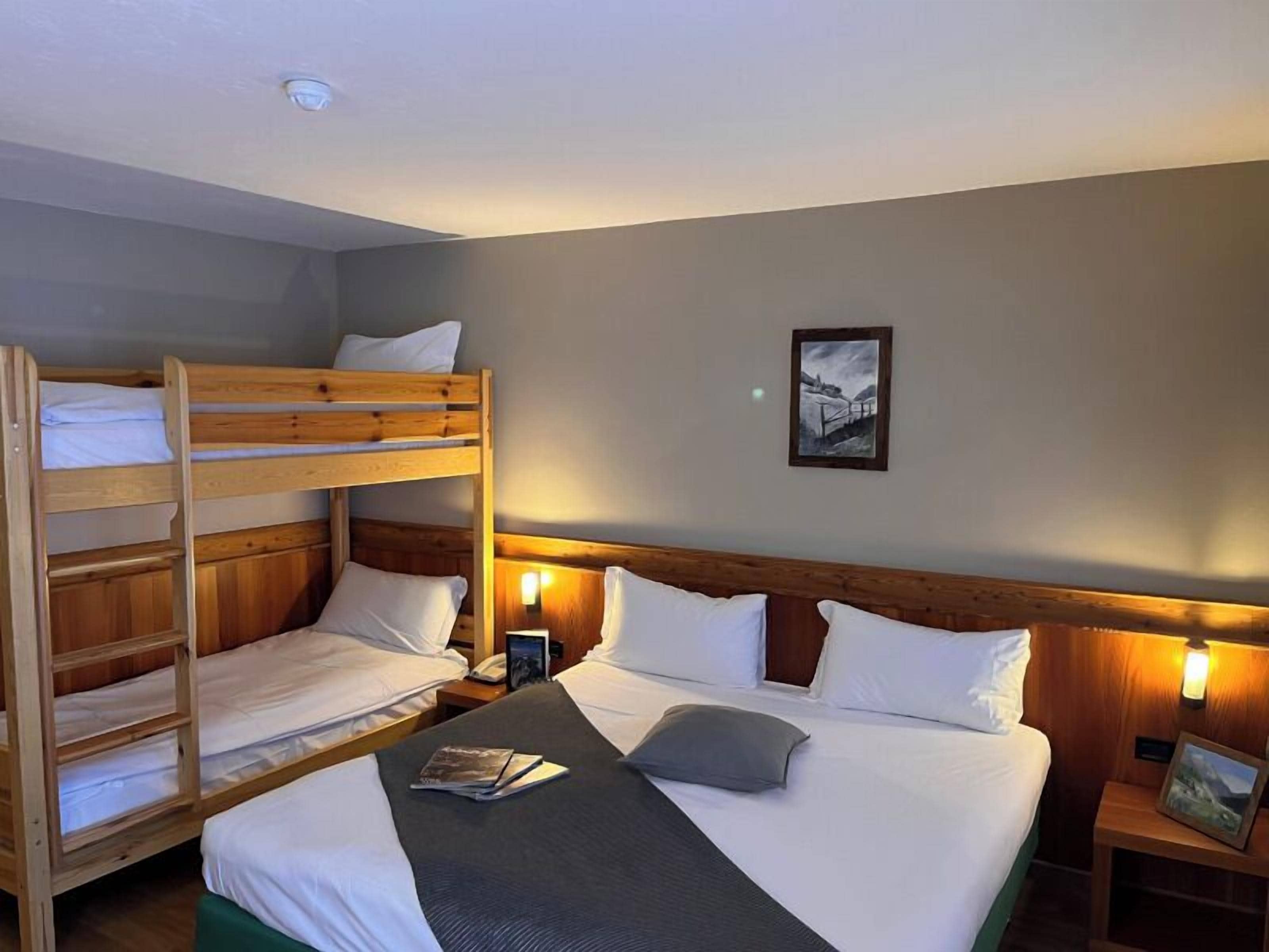 Habitación de hotel con literas, una cama individual, lámparas de noche, un cuadro enmarcado en la pared y una mesita de noche con lámpara.