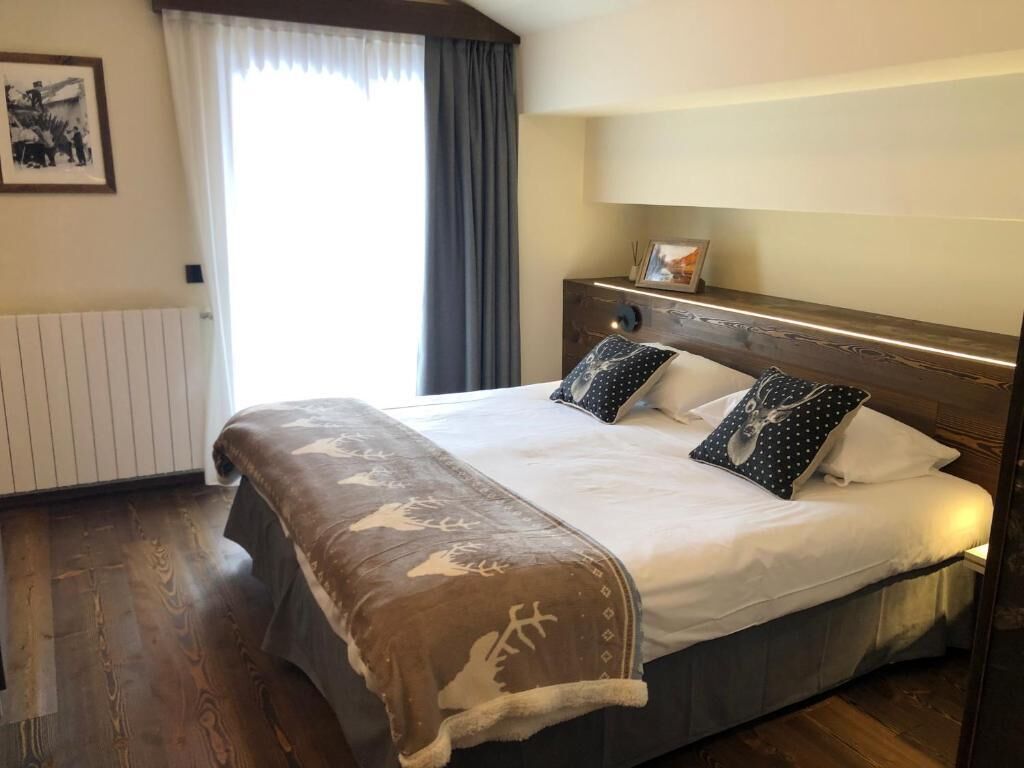 A hotel room with a large bed, a wooden headboard, a bedside table with a lamp, and a window with curtains.