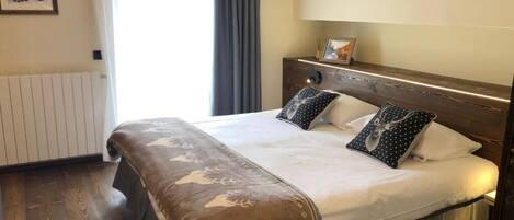 A hotel room with a large bed, a wooden headboard, a bedside table with a lamp, and a window with curtains.