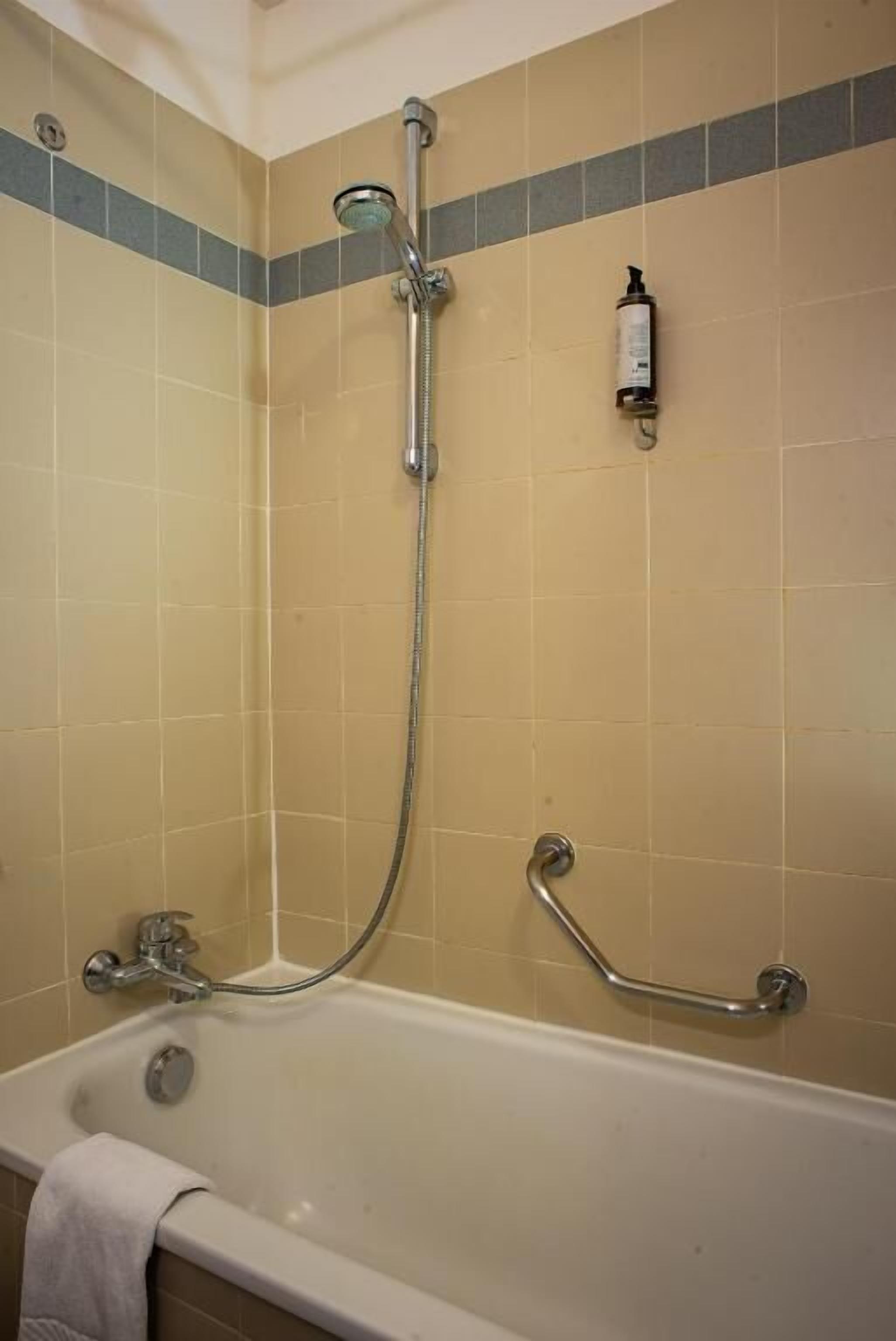 A bathroom with a bathtub, a showerhead, and a handrail.