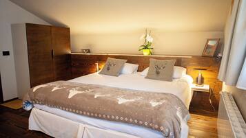 Une chambre à coucher avec un grand lit, une tête de lit en bois, des tables de chevet, une petite table, une plante en pot et un tableau encadré au mur.