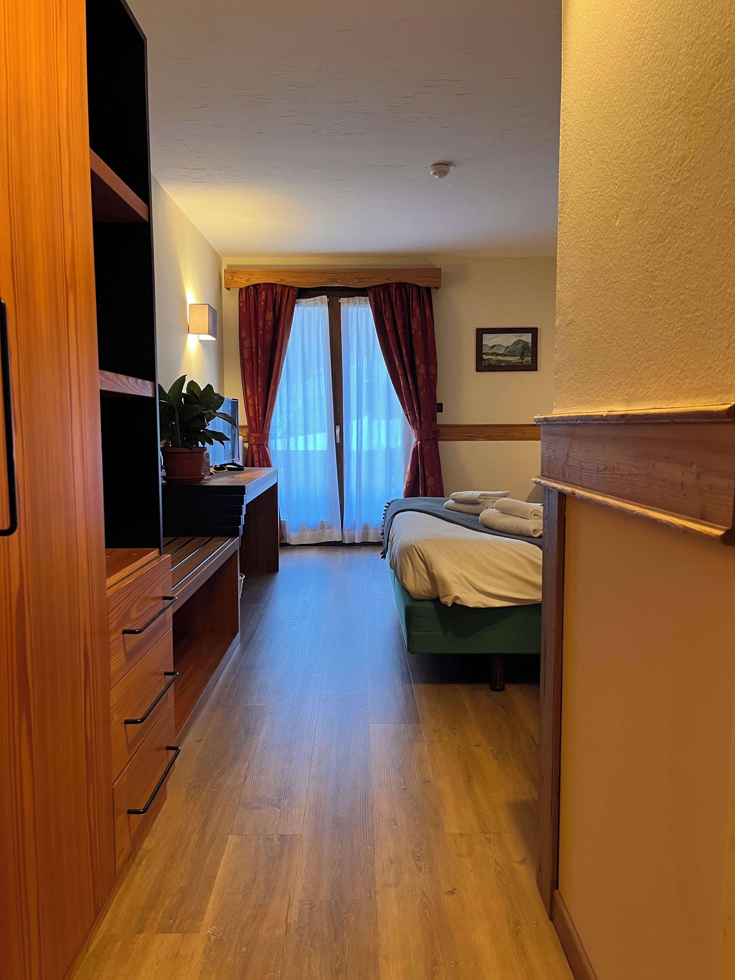 Un corridoio stretto che porta a una camera da letto con un letto, una scrivania e una pianta in vaso.