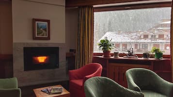 Una sala de estar acogedora con chimenea, un sillón rojo, sillones verdes y vistas a un paisaje nevado a través de una ventana.