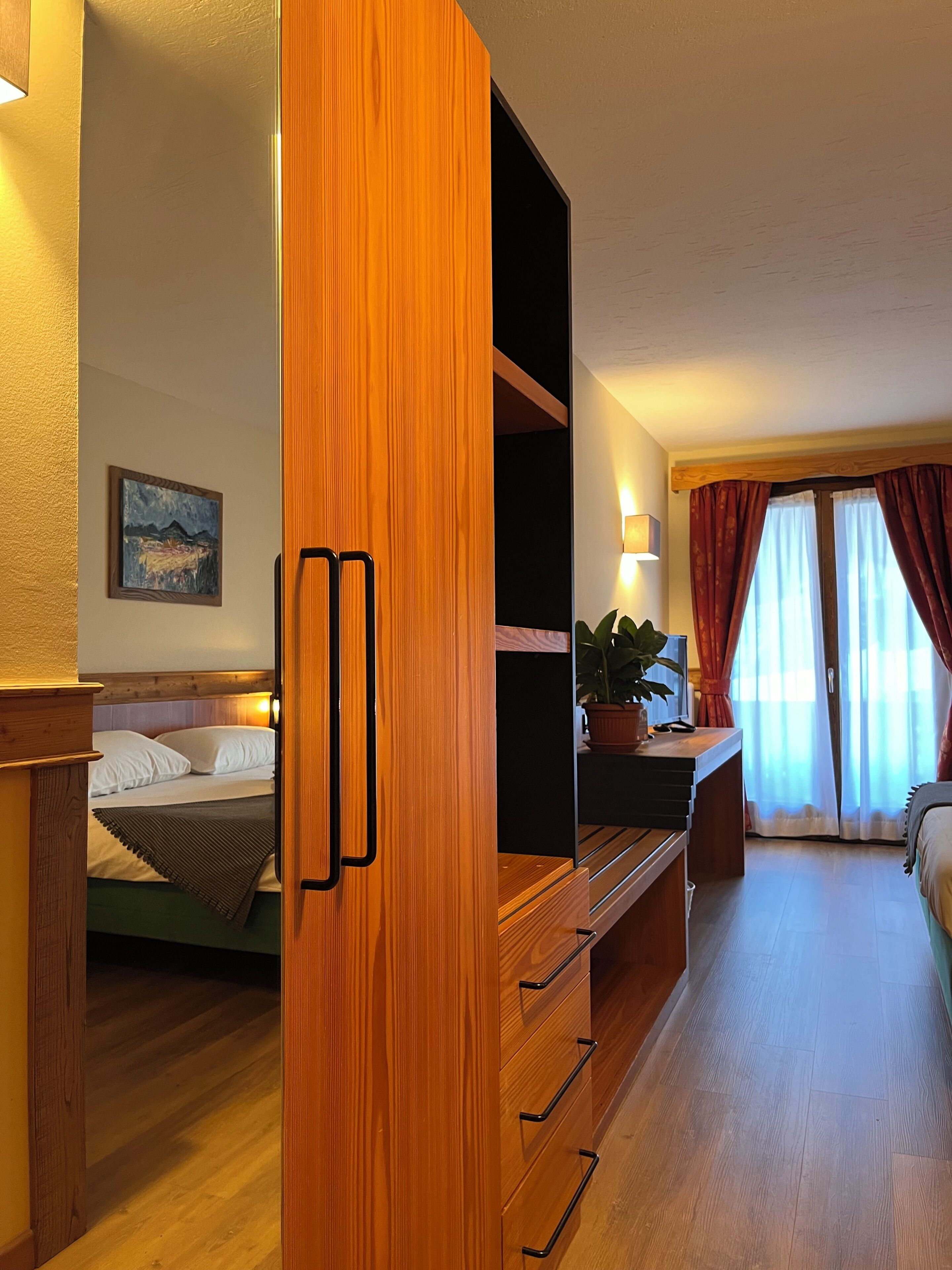 Habitación de hotel con cama, escritorio, planta en maceta y un cuadro en la pared.