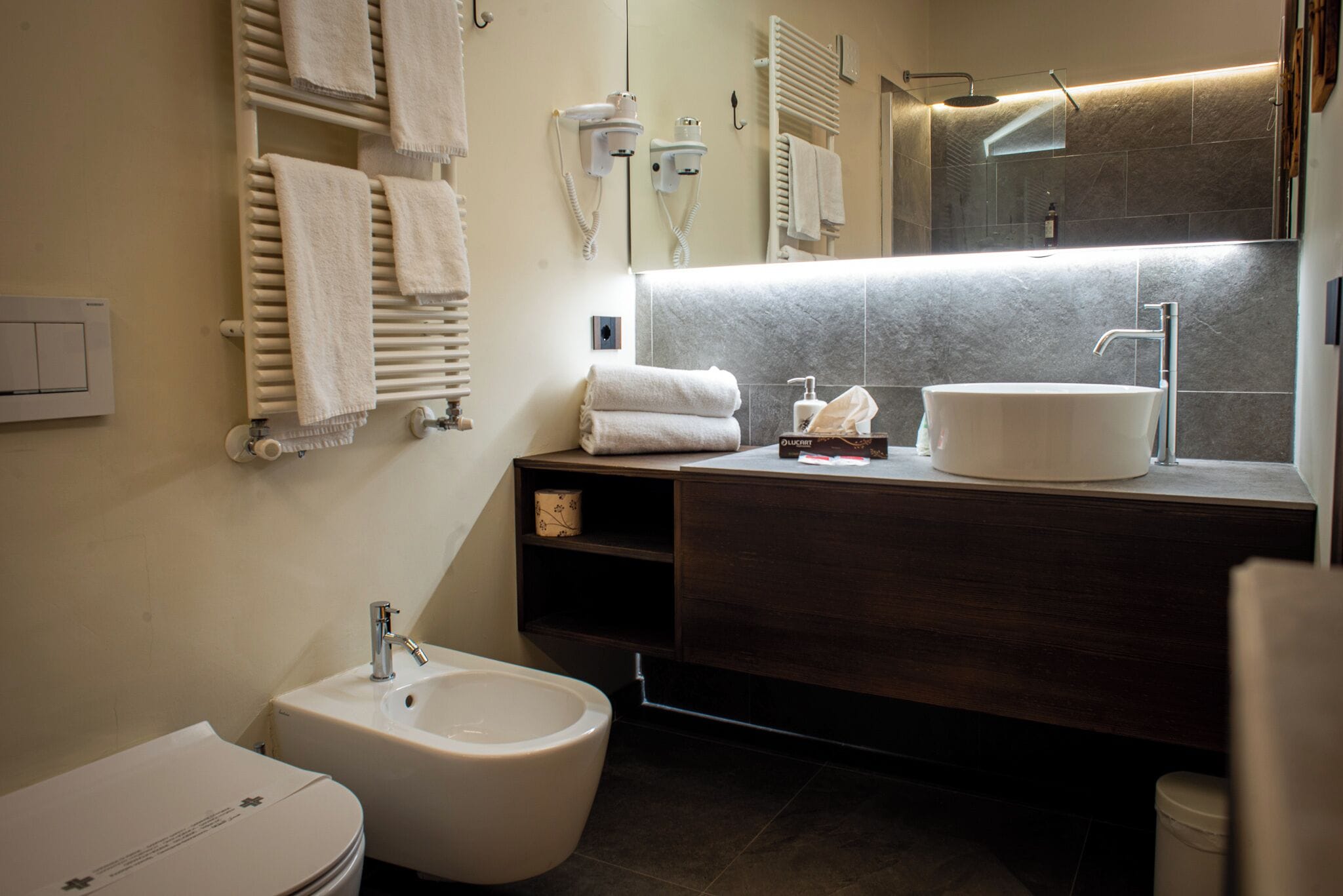 Ein modernes Badezimmer mit einer Bidet, einem Waschbecken mit Spiegel und Handtüchern an einem Halter.