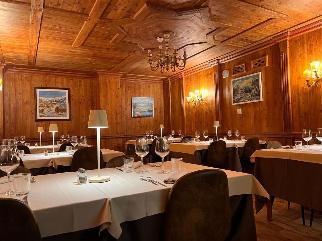 Een eetruimte met meerdere tafels, elk gedekt met wijnglazen, bestek en een lamp.