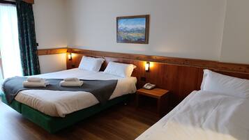 Camera d'albergo con due letti, una testiera in legno, un quadro appeso e un comodino con un telefono.
