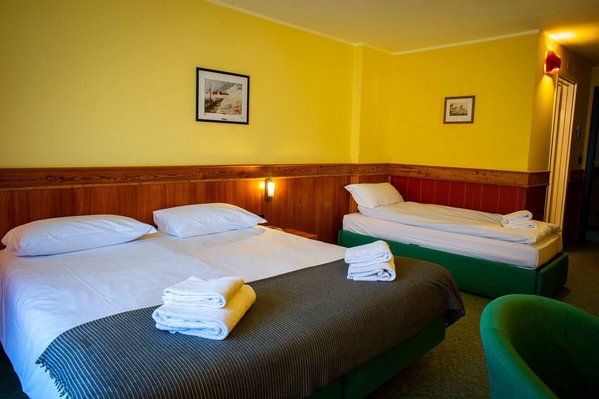 A hotel room with two beds, a green chair, and a wooden headboard.