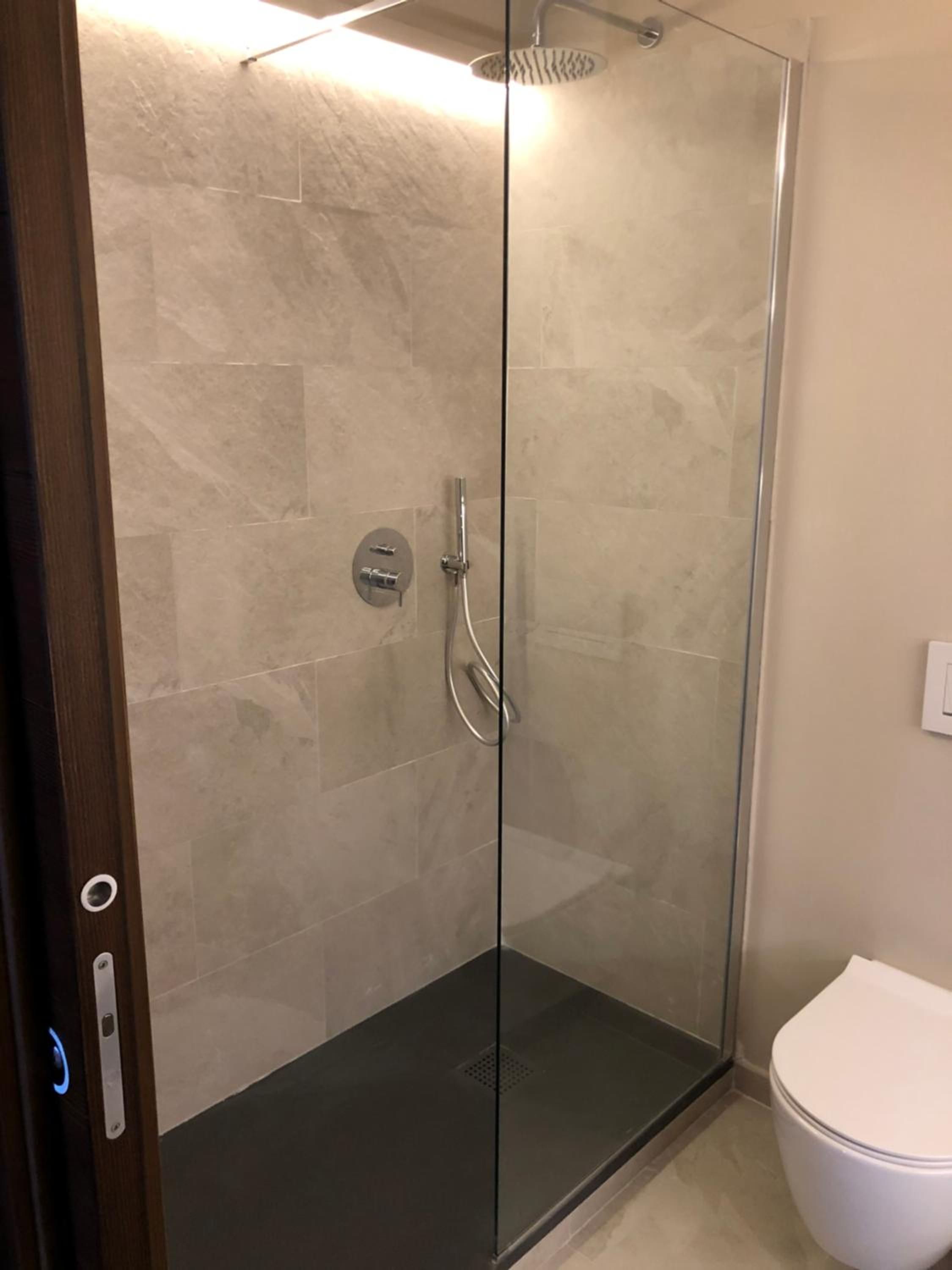 Cabina doccia con pareti in vetro, soffione a mano, rubinetto a parete e, alla destra, il water.