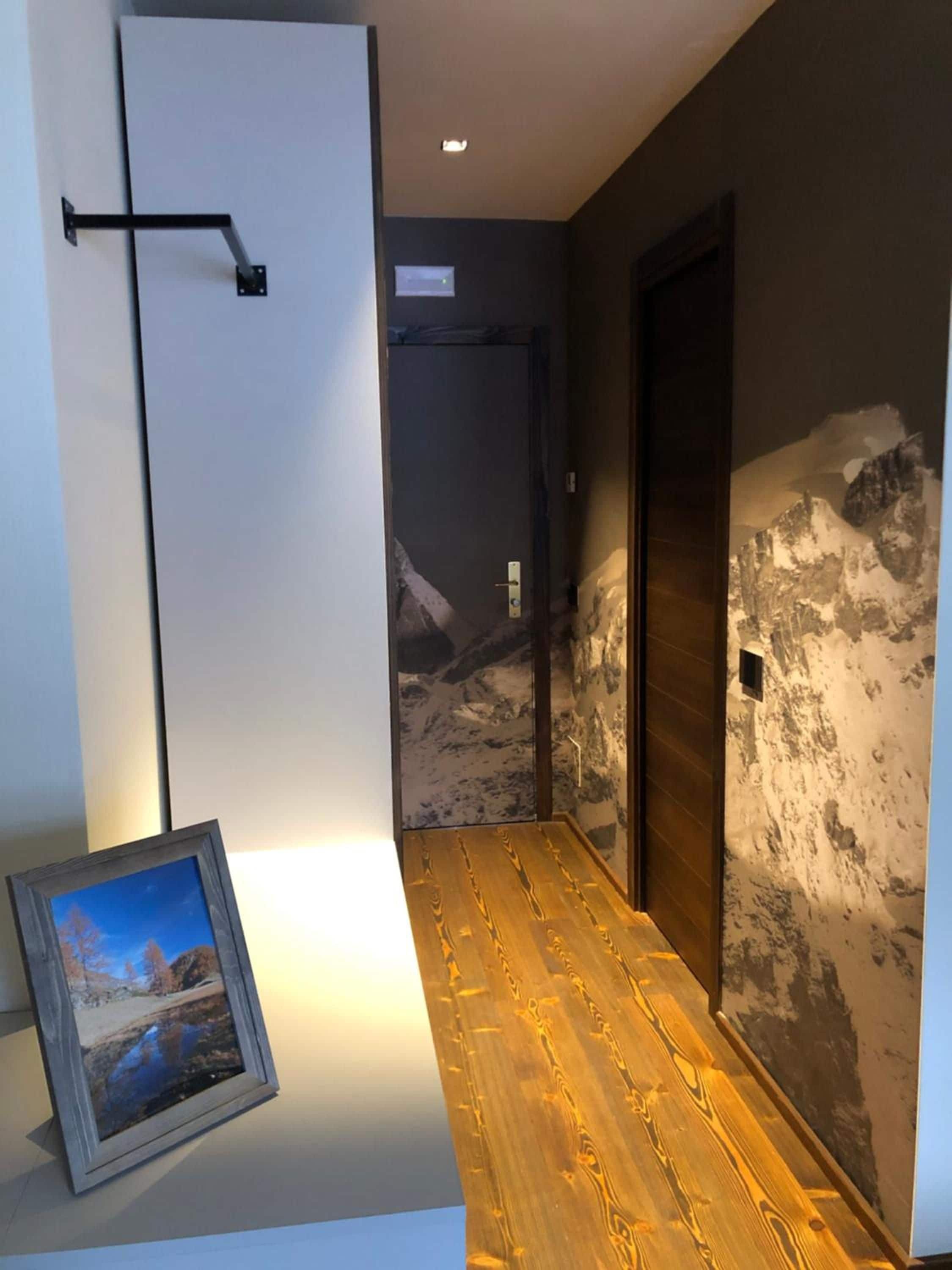 A hallway with a wooden floor, a door with a mountain mural, and a framed picture on the wall.