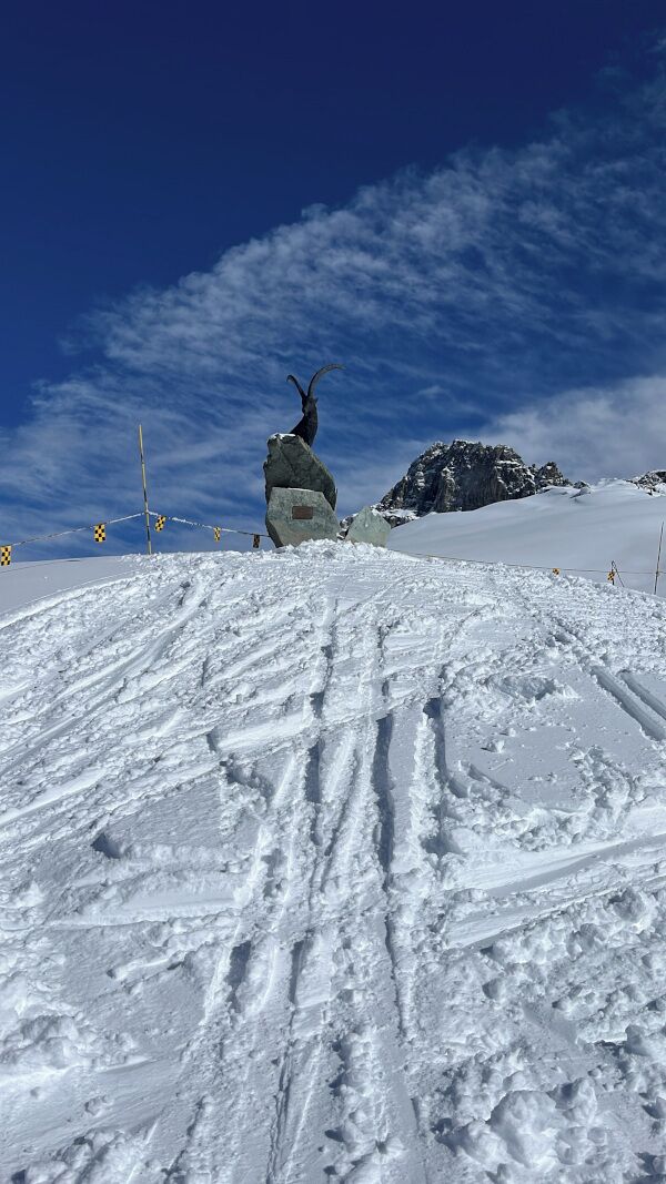 A snowy mountain slope with a large rock formation and a clear blue sky.