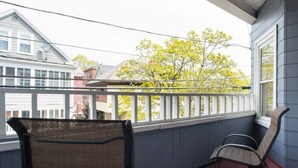 A balcony with two wicker chairs, a red floor, and a view of a tree and neighboring houses.