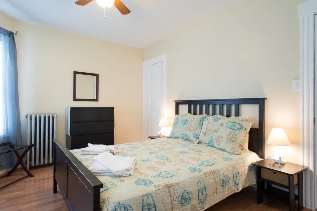 A bedroom with a bed, a nightstand, a chair, a radiator, and a ceiling fan.