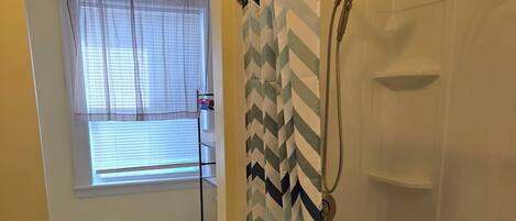 A bathroom with a shower, toilet, and a window with blinds.
