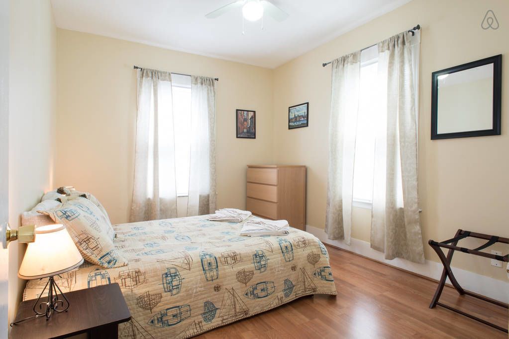 A bedroom with a bed, bedside table, lamp, and curtains.