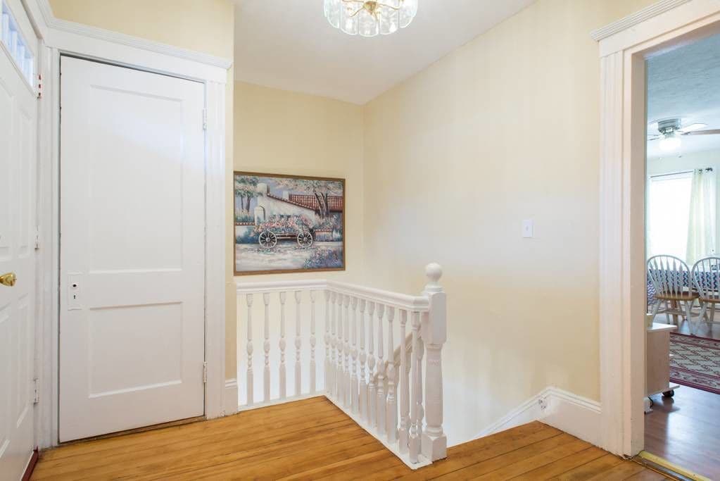 A hallway with a white door, a painting of a bridge, and a white railing.