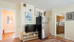 A compact kitchen with a refrigerator, a television on a stand, and a wooden cabinet.