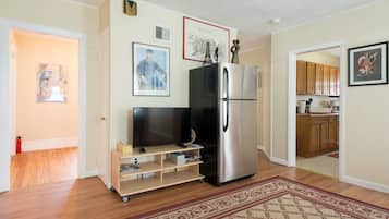 A compact kitchen with a refrigerator, a television on a stand, and a wooden cabinet.